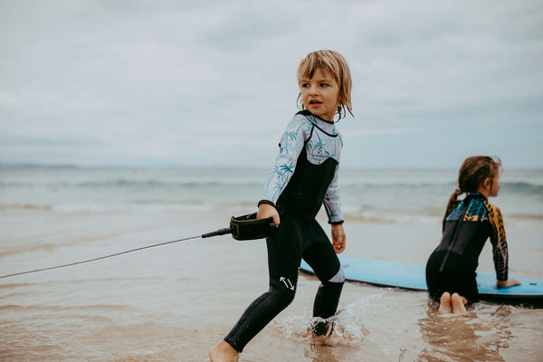 Kids in wetsuits playing with surfboards