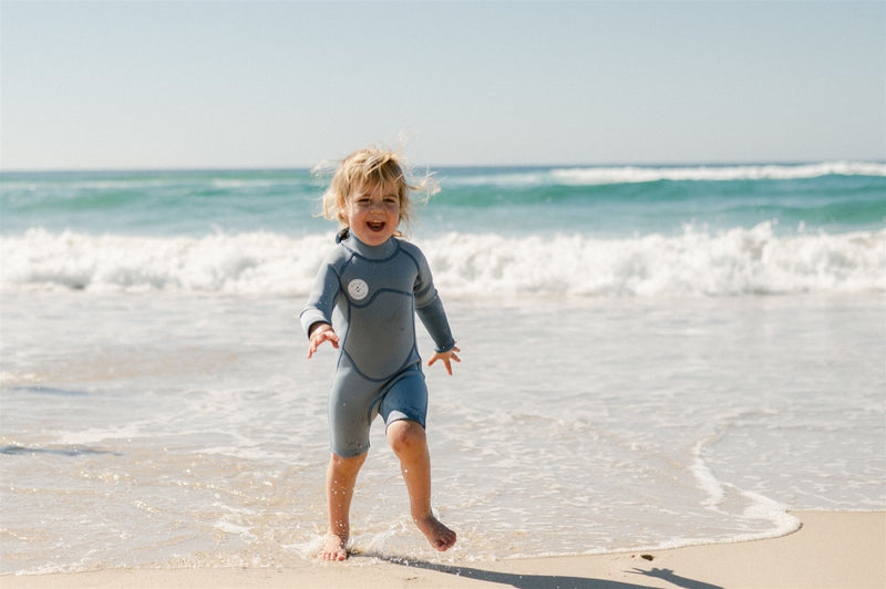 Girl running on the sand smiling in her kids long-sleeve wetsuit.
