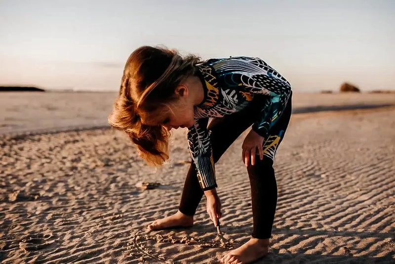 Girl playing in sand in wetsuit