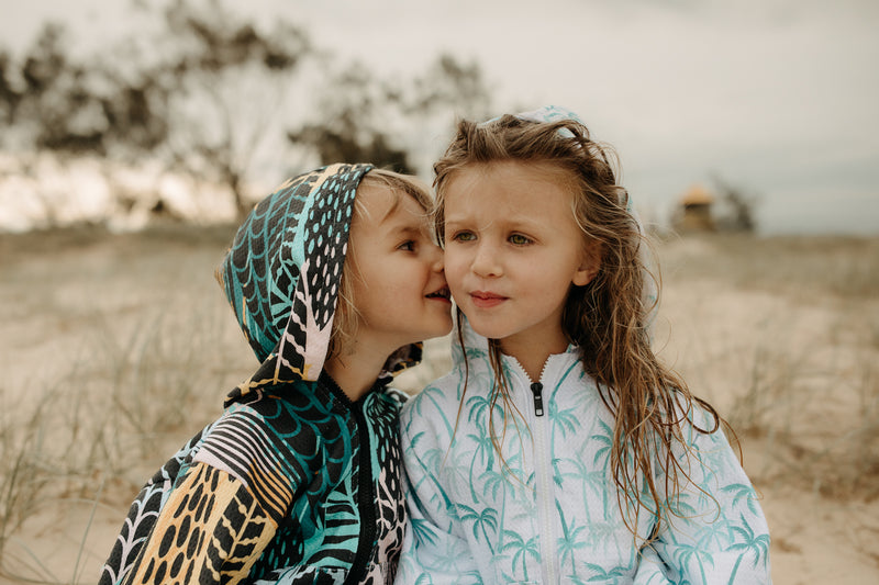 Girl and boy whispering on beach in hooded towels