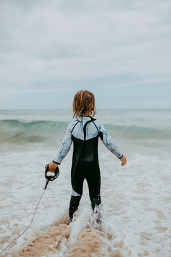 Boy looking at waves in kids full length wetsuit